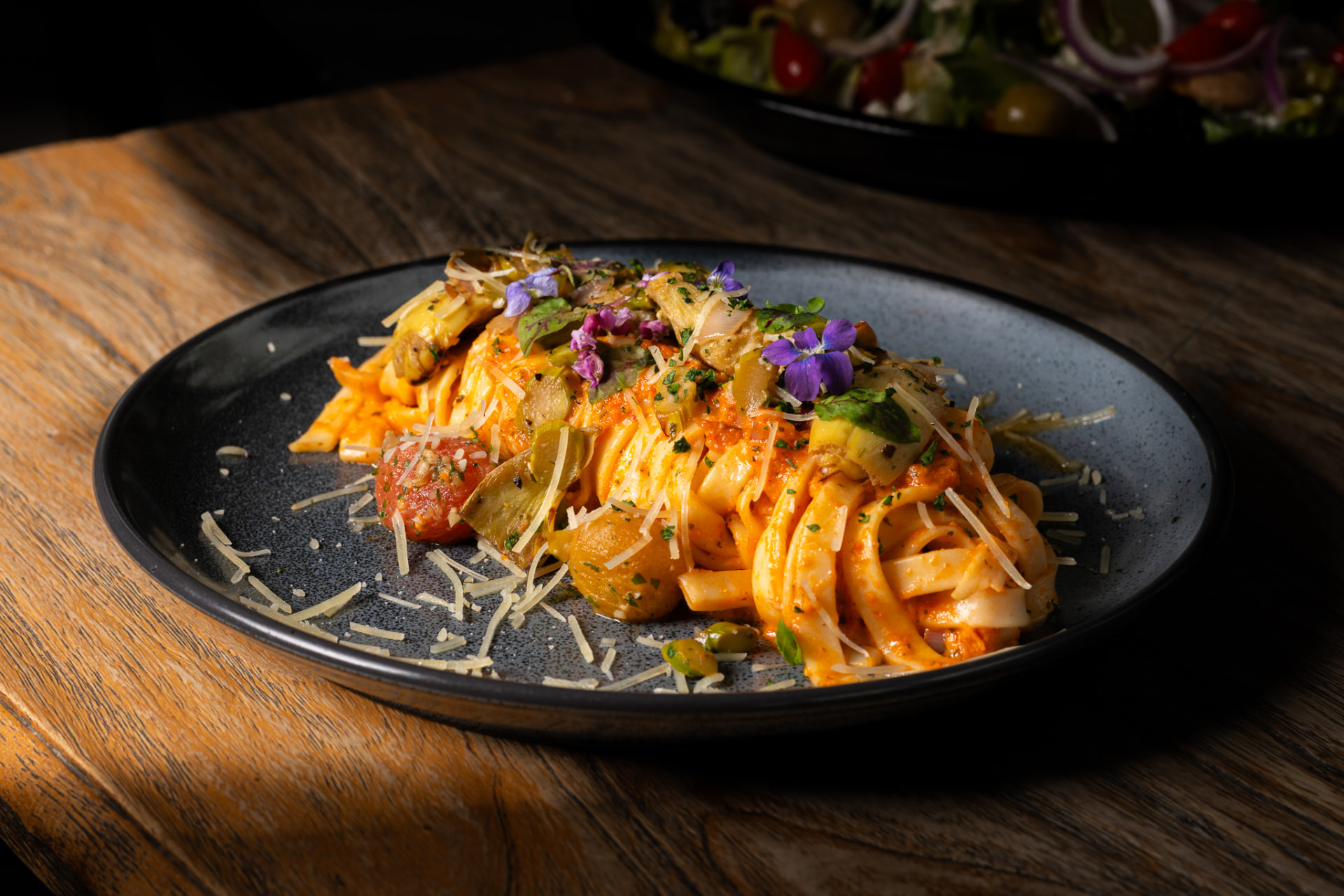 Fettuccine with artichokes and edible flowers on a dark plate