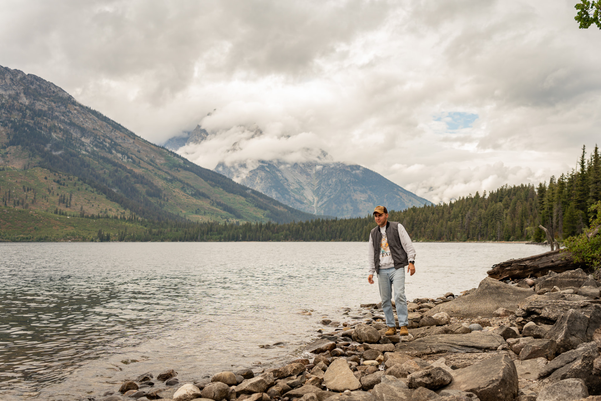 Man walking the rocky shoreline of a mountain lake under clouds