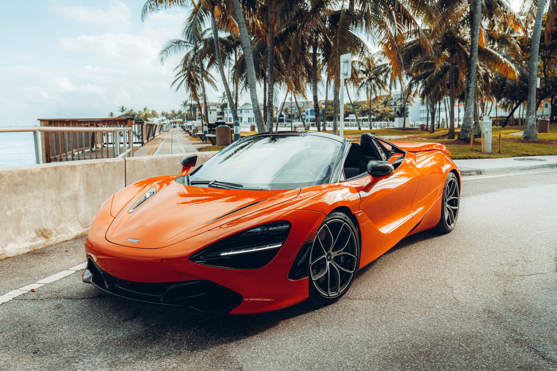 Orange McLaren 720S Spider along a palm-lined waterfront