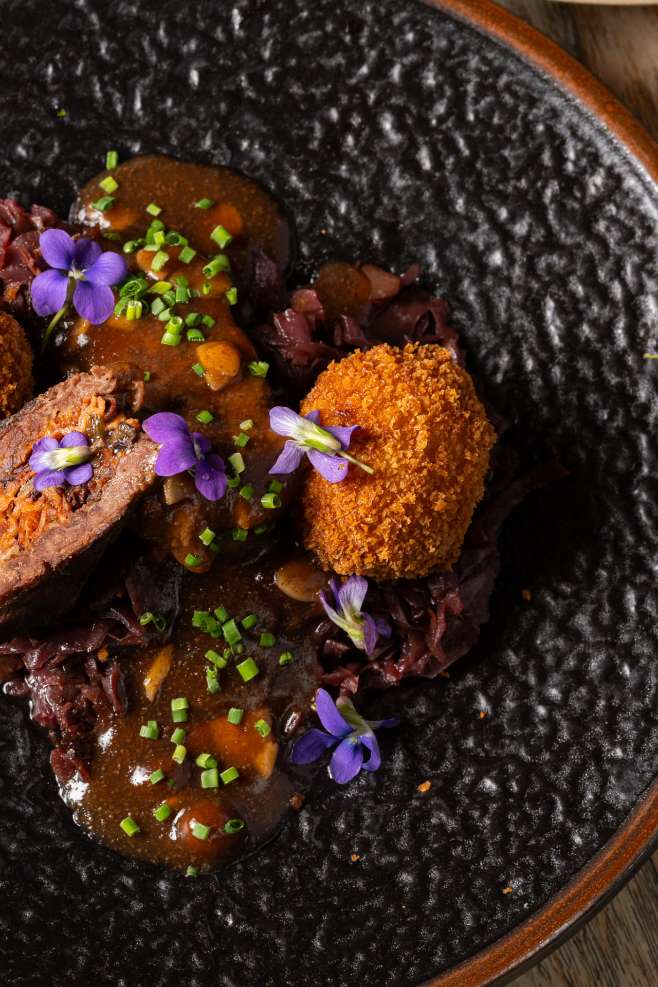 Braised beef with croquette and violets on a black plate